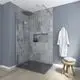 Dusche mit modernen grauen Fliesen und einer Glasabtrennung. Vor der Wand hängen ein Bademantel und ein Handtuch. Badearmatur von Ideal Standard sichtbar.